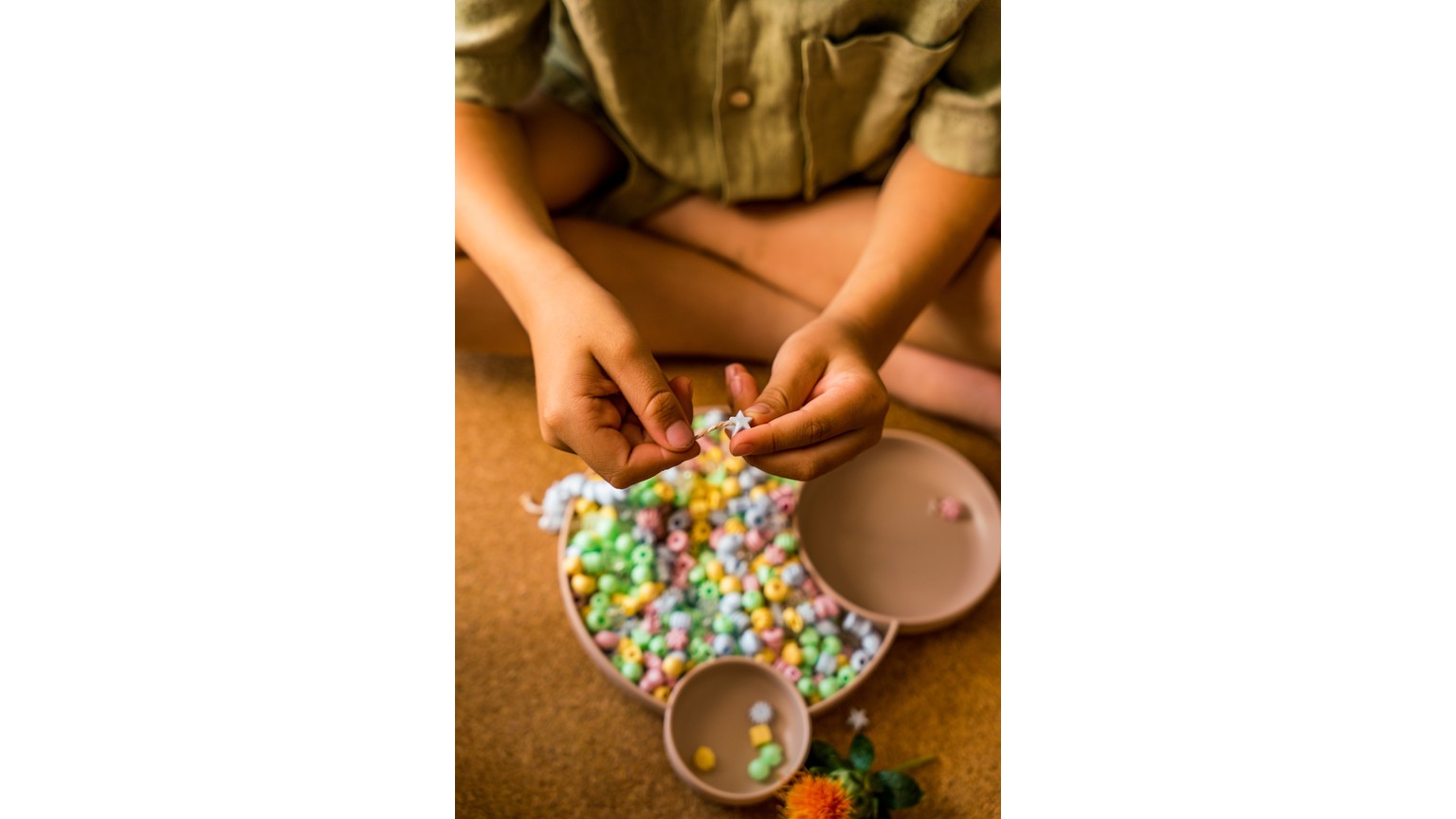 Hænder sorterer små farvede perler på en rund plade med brune drikke ved siden af.
